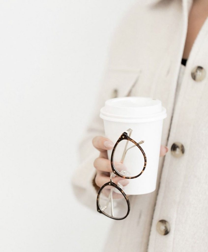 Woman holding glasses and takeaway coffee cup, representing balancing home, work and festive responsibilities