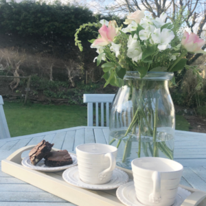 two cups and a vase of flowers outside on a table 