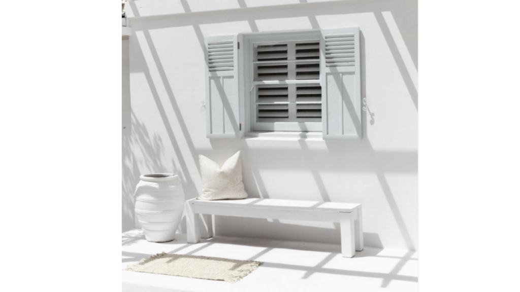 white bench underneath a window with pale blue shutters in the sunshine