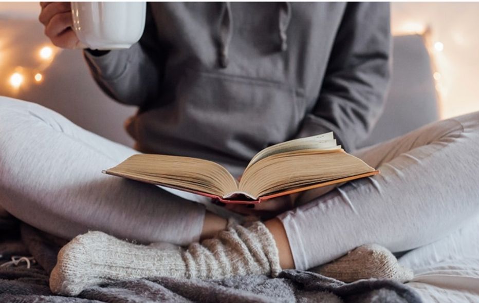 image of lady sitting cross legged reading with a mug of hot drink 