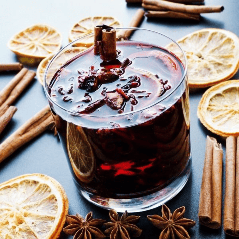 Glass of mulled wine surrounded by cinamun sticks and orange slices