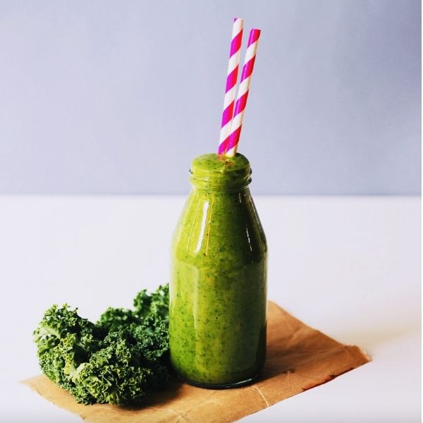 Bottle of green smoothie with a straw, broccoli on the side 